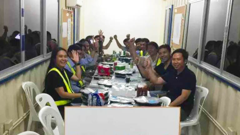 Construction workers smiling to the camera while sitting at a table having lunch