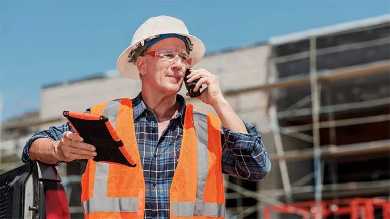 Contractor having a conversation on the phone while holding a tablet standing on site
