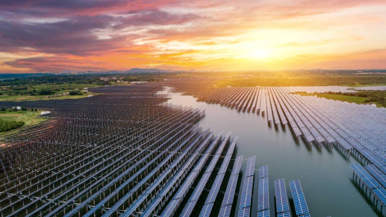 Aerial view of solar panels on a lake with the sun rising in the background