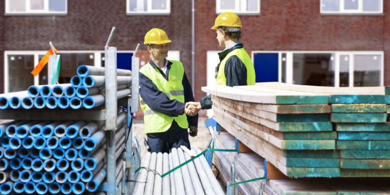 Photo of two contractors shaking hands next to stacks of construction materials