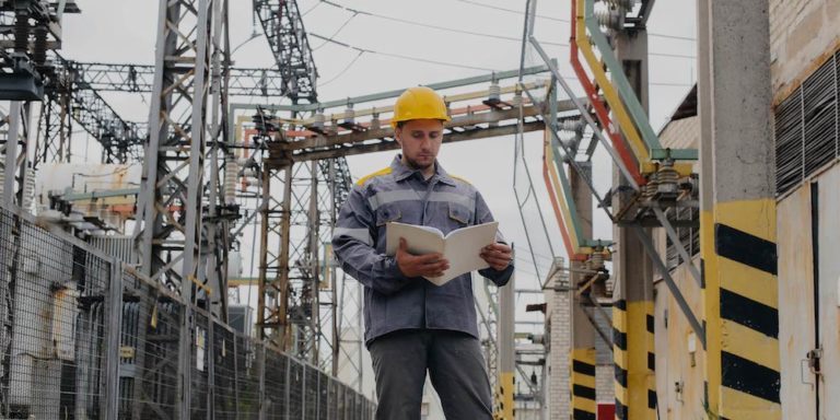 Man in hard hat reviews document in front of electrical station.