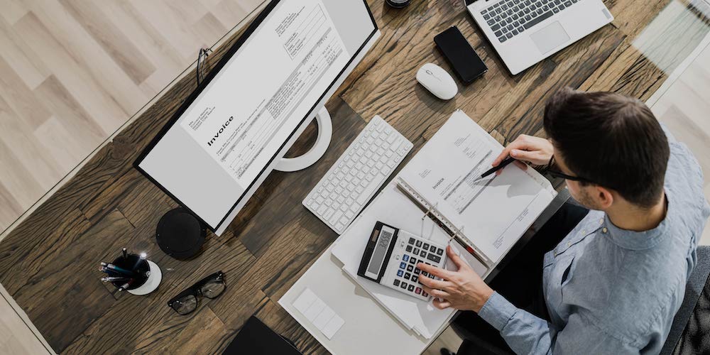 Overhead shot of a man sitting at a desk reviewing invoices.