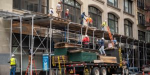 Construction workers unload material from a truck to other workers standing on scaffolding.