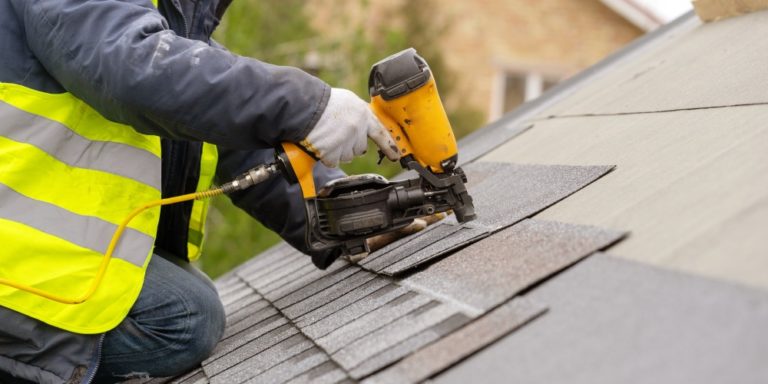 Contractor installing asphalt shingles on a roof with a nail gun.