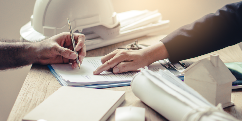 Close up of person's hand signing a contract with another hand pointing to the document.