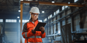 Contractor wearing protective hard hat, eyewear, and reflective vest examining clipboard with safety documents