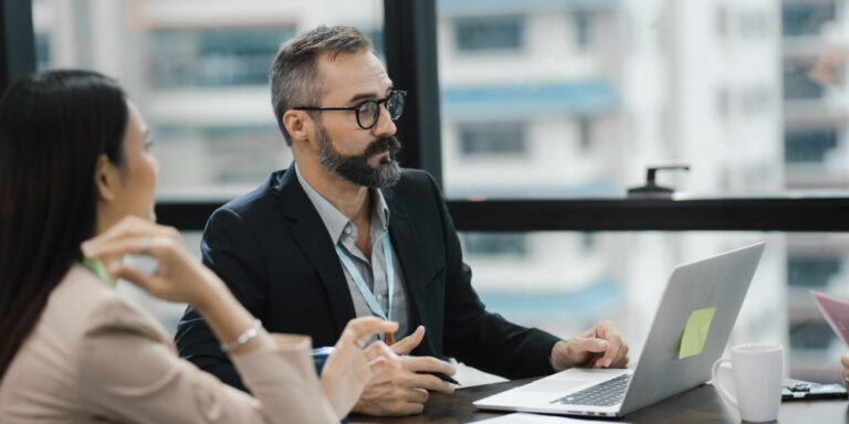 Photo of 2 people in a office reviewing a document on a laptop.