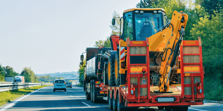 Construction mobilization illustrated by large equipment being transported down a road