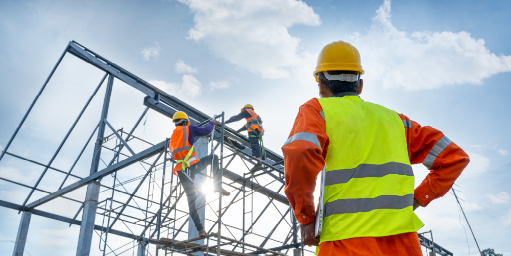 Two construction workers with harnesses, high-viz vests, and hard hats climb a scaffold while a third watches