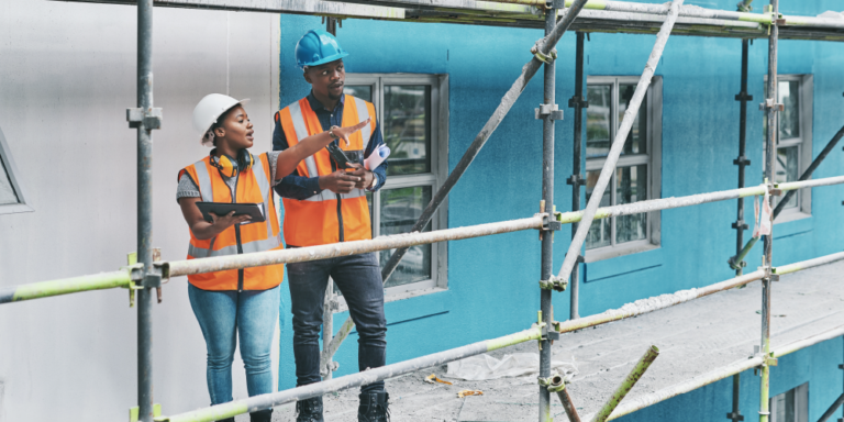 2 construction workers on a jobsite completing a construction safety report on a clipboard.