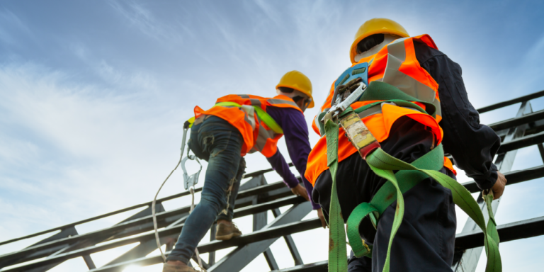 Construction workers scaling scaffolding while wearing safety equipment including protective hardhats and harnesses
