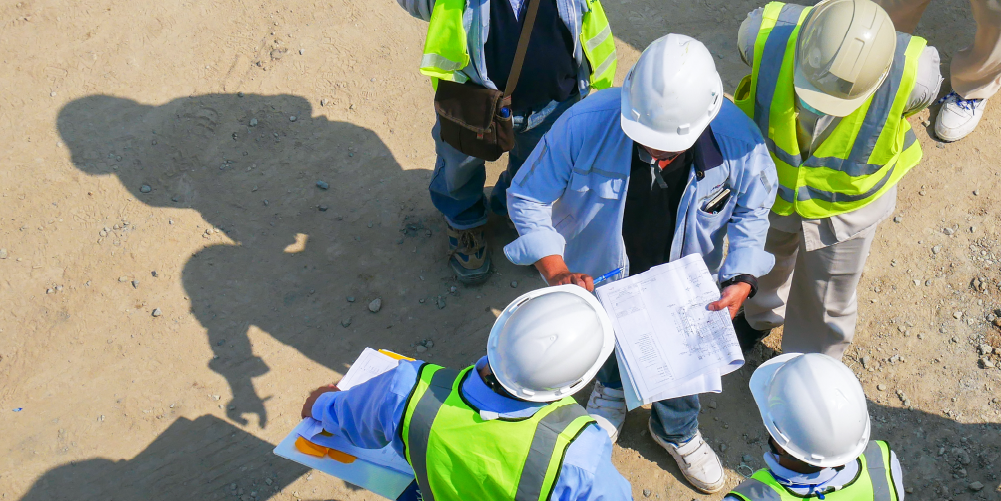 Photo of inspector with paperwork talking to other workers wearing hard hats