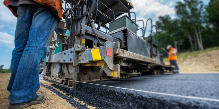Contractor stands next to paving machine laying new asphalt on a road construction project.