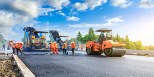 Photo of workers supervising a steam roller on a road construction project