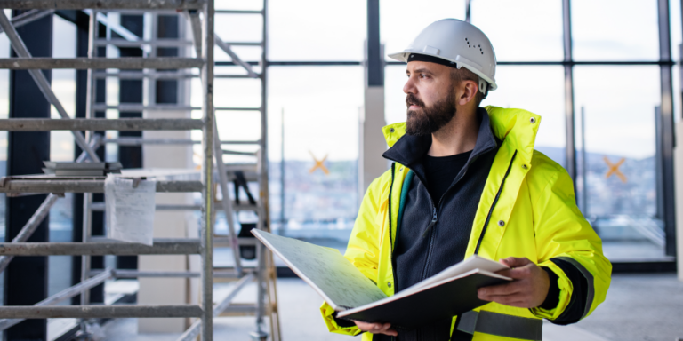 A contractor on a jobsite is holding a book of documents.