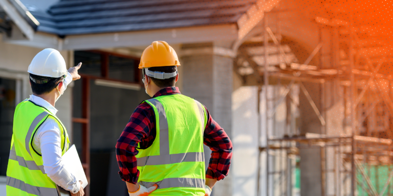 2 workers wearing reflective vests and hard hats discussing a construction safety management plan on a site