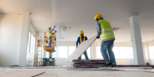 Three construction contractors install drywall inside of a building.