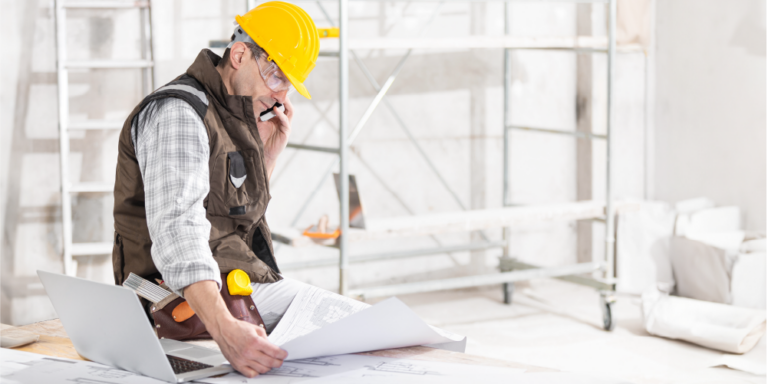 Photo of a construction professional looking at drawings and talking on the phone.