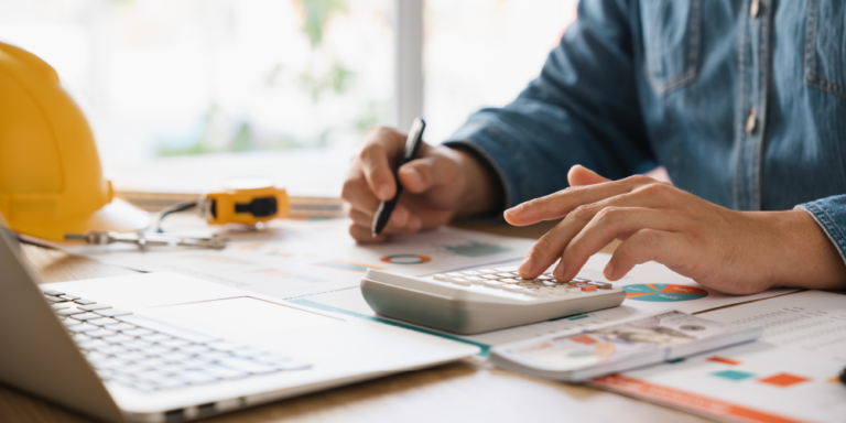 Photo representing the balance sheet in construction by showing someone using a calculator to work on construction documents