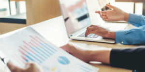 Managing cash flow in construction illustrated by an up close photo of 2 people's hands as they look at financial reports and laptops