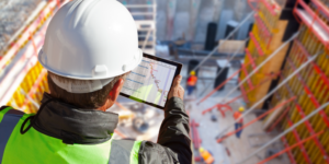 Photo of a construction professional looking at construction finance data on a tablet while overlooking a construction site