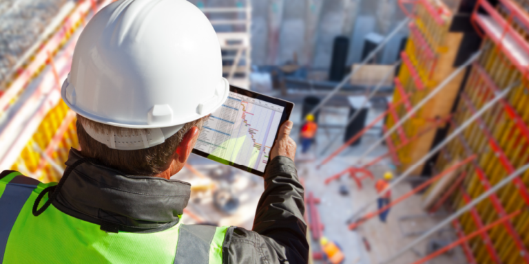 Photo of a construction professional looking at construction finance data on a tablet while overlooking a construction site