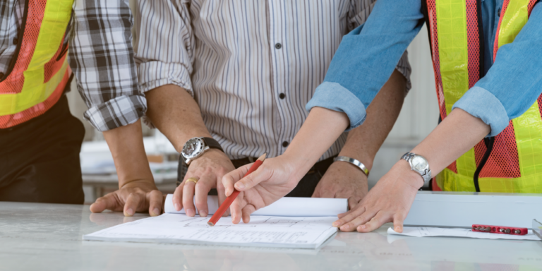 Up-close photo of 3 construction professionals reviewing feasibility study paperwork