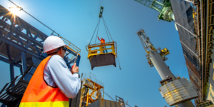 Photo of construction worker looking upward at a load being lowered by a crane.