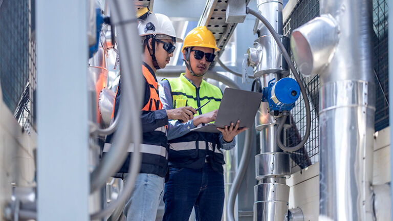 Workers on a jobsite in PPE looking at a laptop