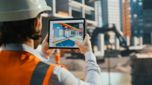 Construction worker comparing a jobsite to a 3D model of the jobsite on a tablet