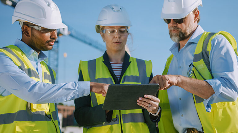 3 workers gathered around a tablet on a construction site