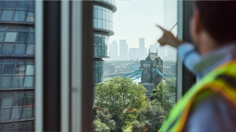 A man in hi-vis jacket points at tower bridge in London.
