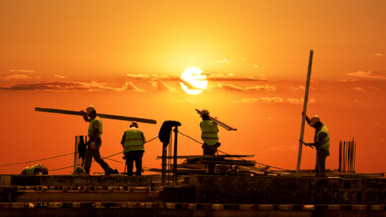 Workers on a construction site backlit by a sunrise