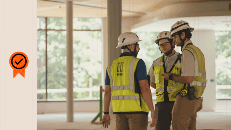 Photo of 3 workers in PPE in an unfinished room of a jobsite with a safety icon on the left side