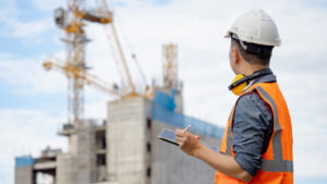 Worker monitoring construction site activities and recording observations on a tablet