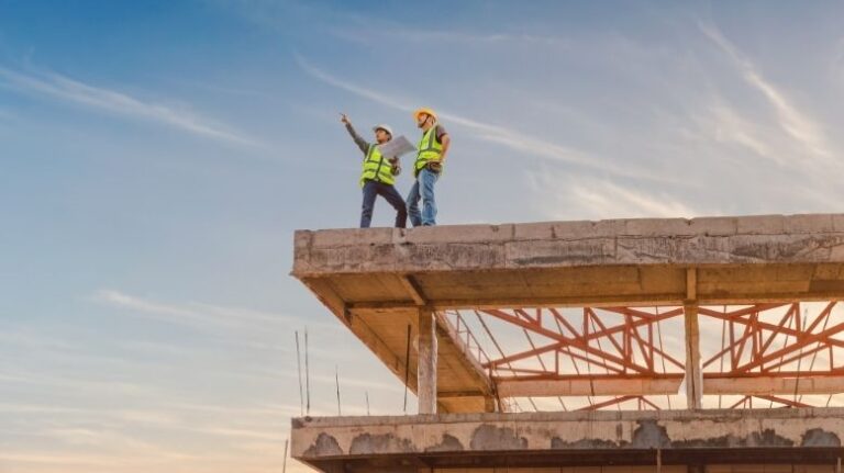 Two construction workers on top of a structure looking off into the distance