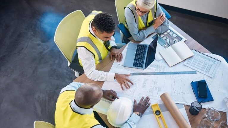 Overhead photo of 3 construction professionals at a table discussing documents and plans