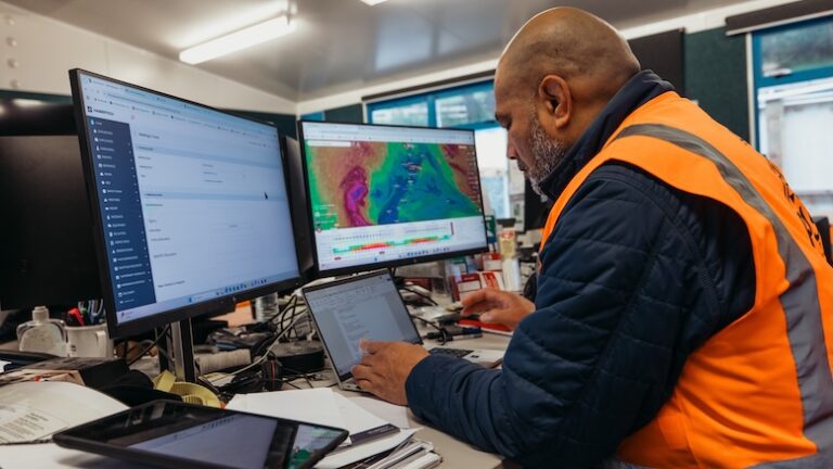 Man in a construction office is checking dashboards across multiple computer monitors