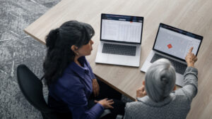 Two workers in an office of a construction project owner looking at portfolio data on laptops